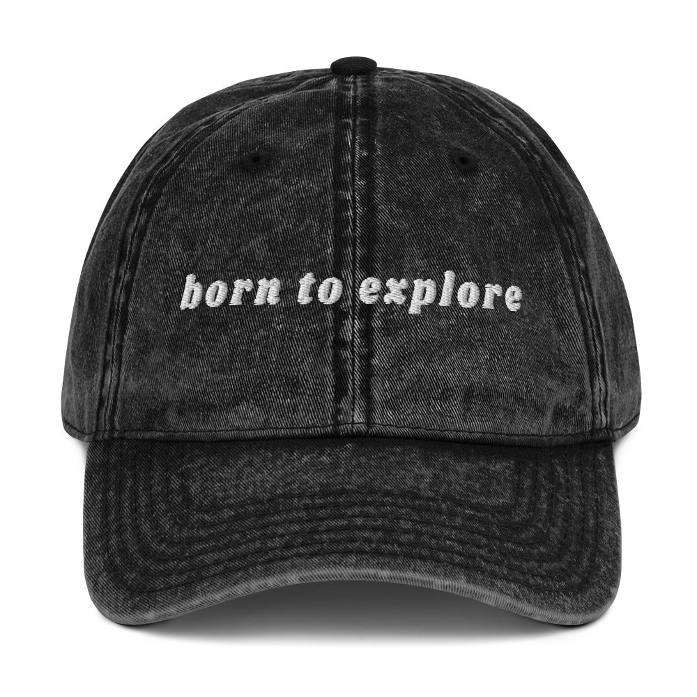 Black denim cap with 'born to explore' text on a white background