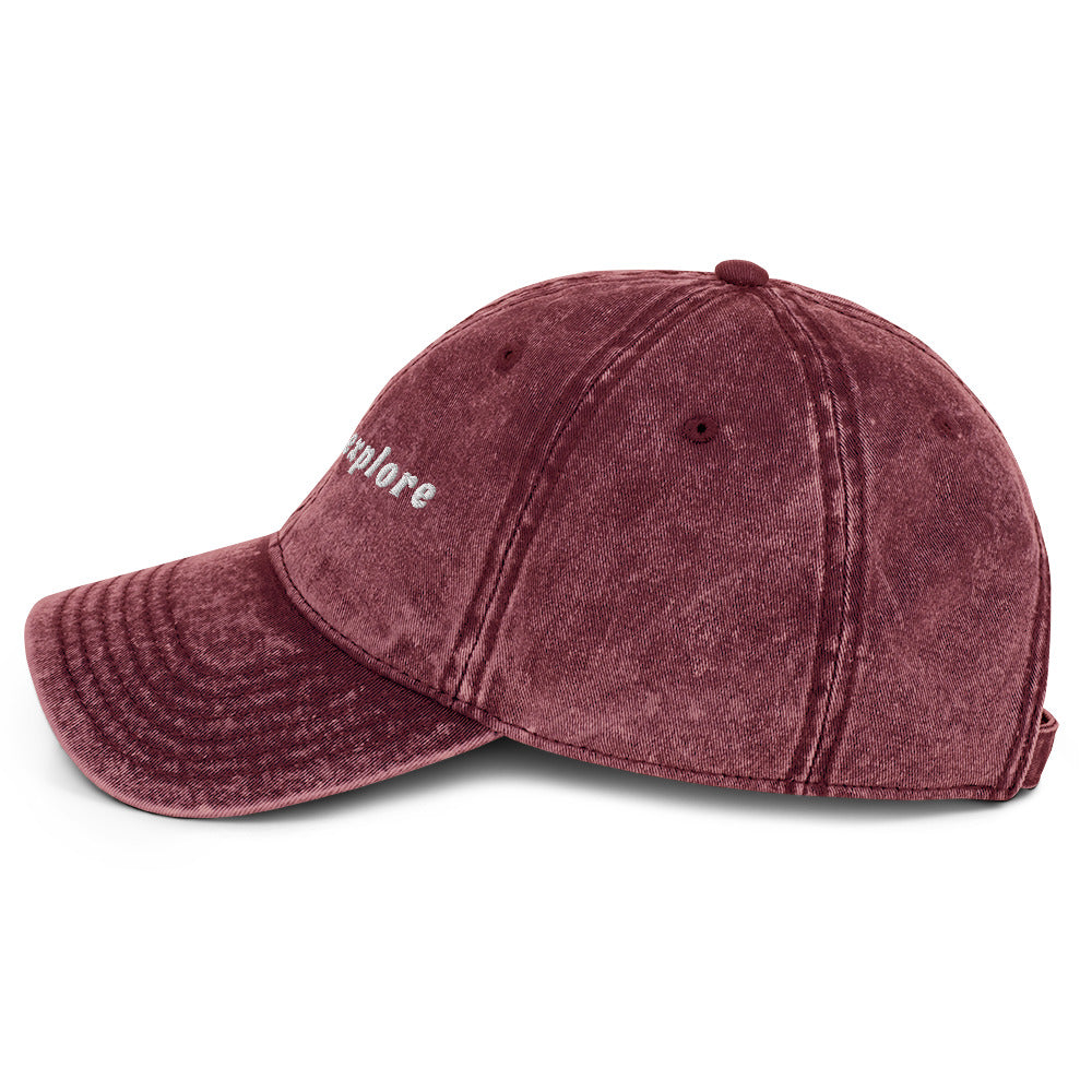Maroon baseball cap with 'born to explore' embroidery on a white background