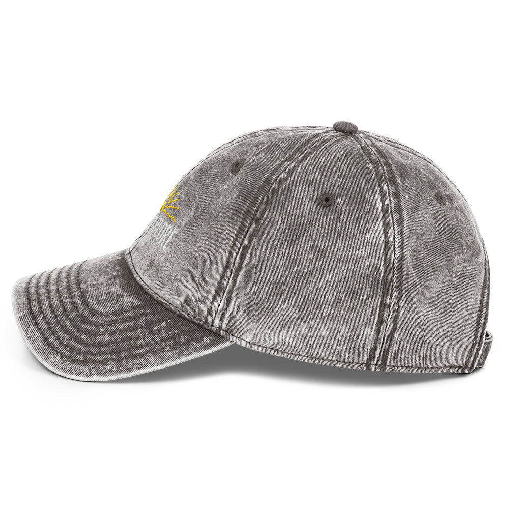 LIght gray distressed baseball cap with a small yellow born to explore logo on a white background
