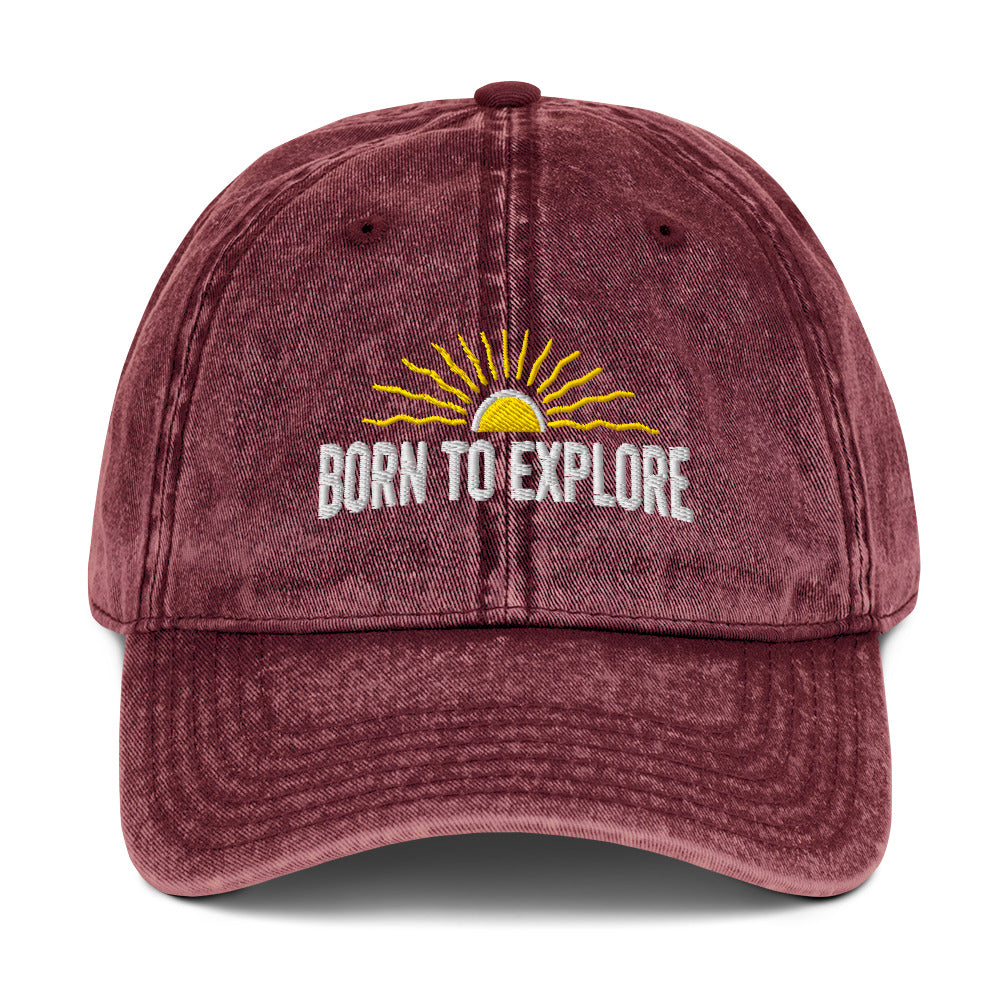 Maroon cap with 'Born to Explore' text and sun graphic on a white background