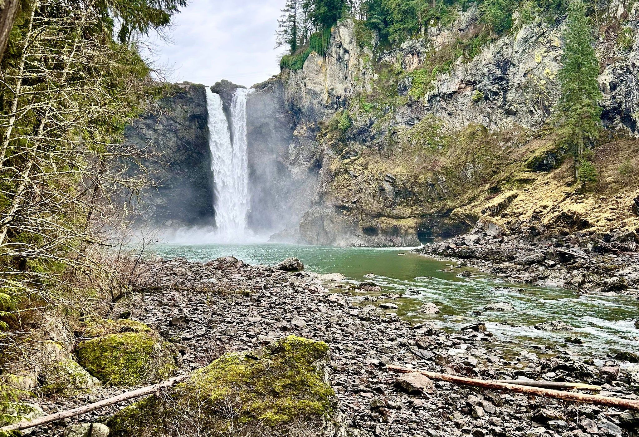 Waterfall cascading down a rocky cliff into a pool surrounded by trees and rocks.